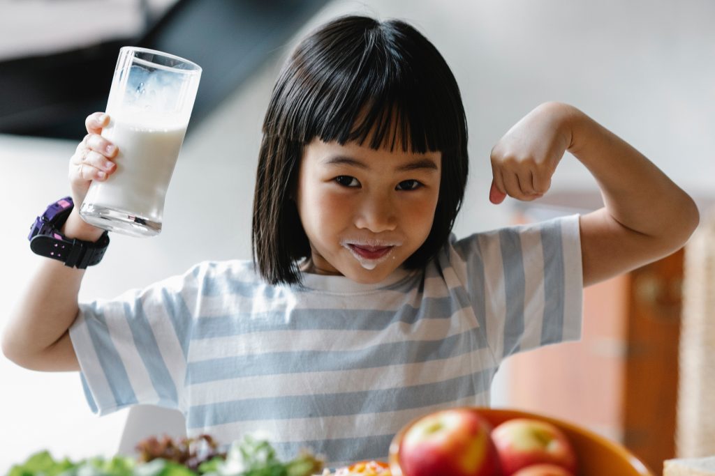 Girl with milk mustache drinking milk and showing muscles for school milk programs.